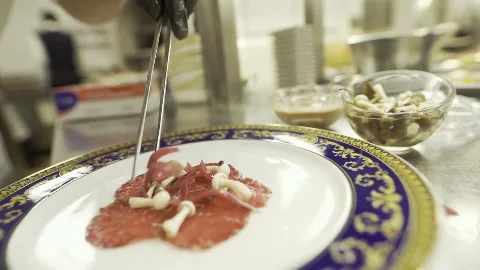 A chef finishing a dish on an ornate blue-and-gold plate.